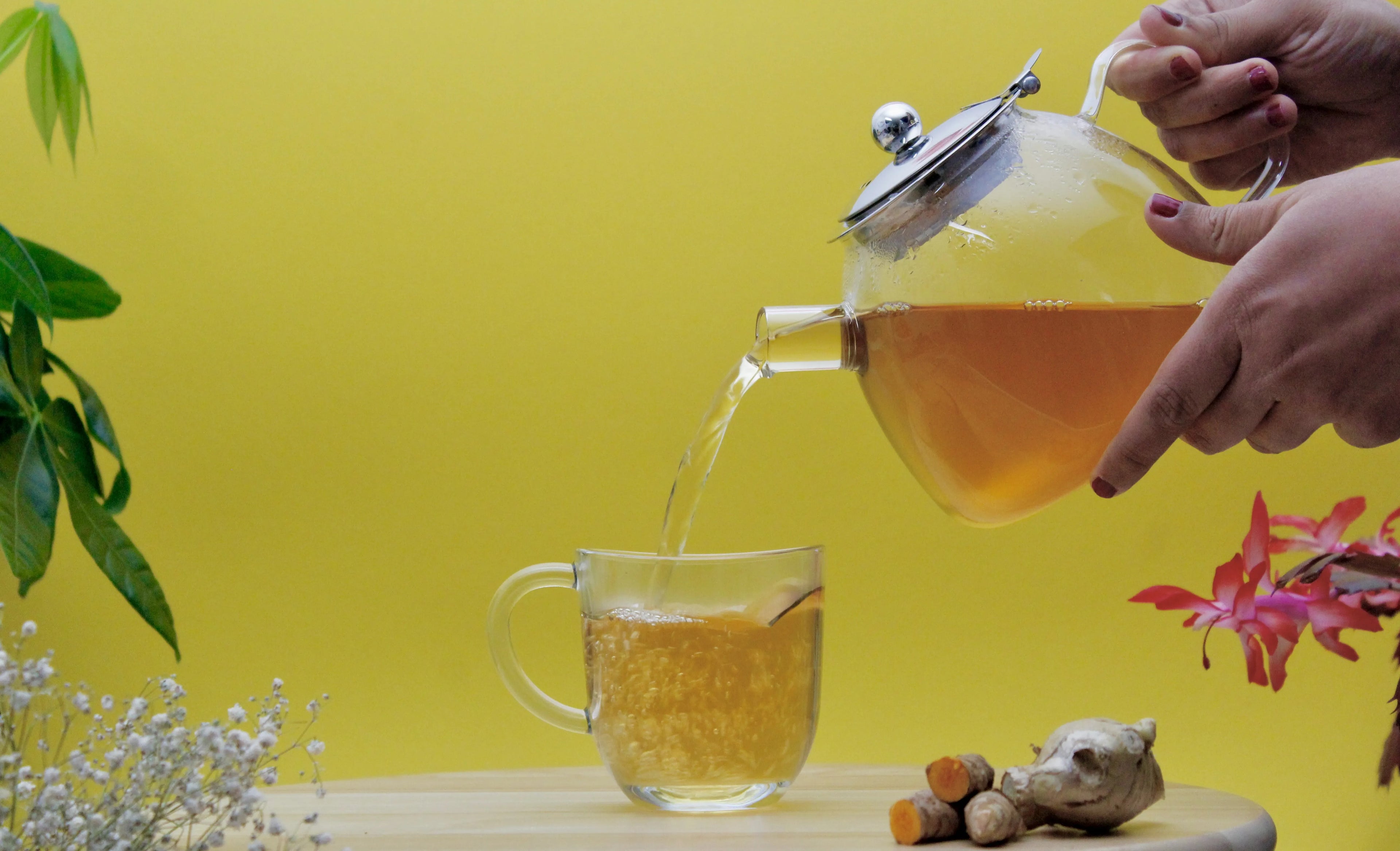 Tee fließt in eine Tasse, mit aromatischem Ingwer und würzigem Kurkuma im Fokus – eine perfekte Mischung für Ayurtea's Wellness Tee